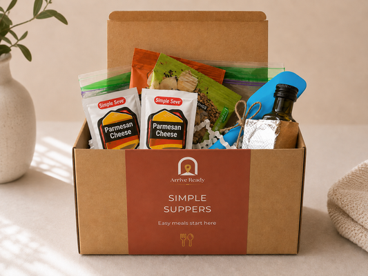 A kraft gift box arrival kit labeled 'Arrive Ready Simple Suppers' filled with packaged food items, including  Parmesan Cheese bags and a small bottle of olive oil, and spices, set on a tabletop with a vase and cloth nearby. Arrive Ready, vacation rental